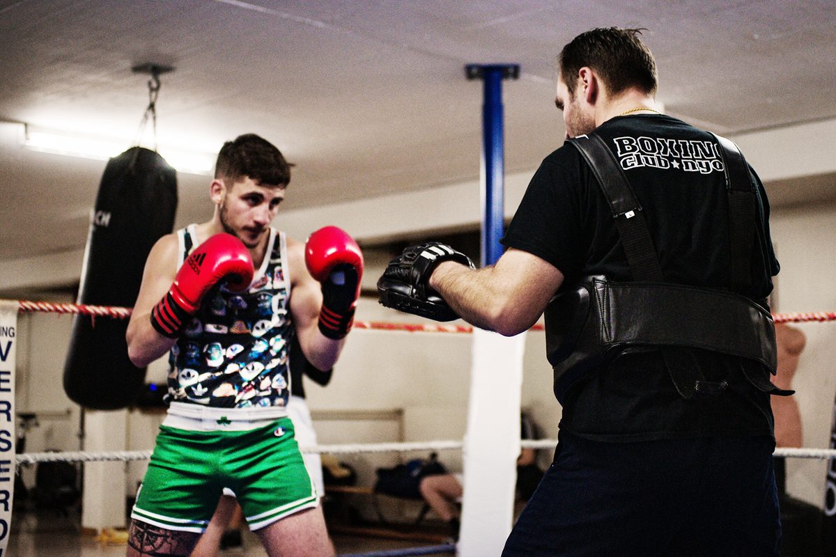 Un entraîneur du club encadre un jeune boxeur pendant un exercice sur le ring